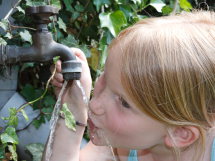 Mädchen trinkt Wasser aus einem Wasserhahn.